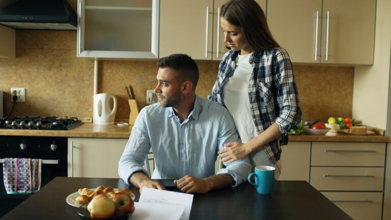 Senior couple reviewing insurance documents, glasses, a pen, and a folder at a kitchen table.