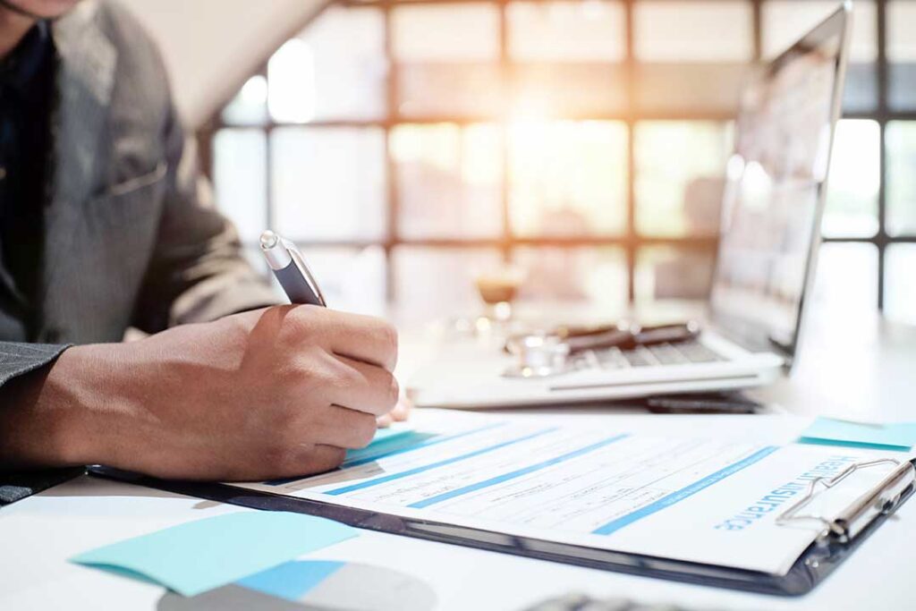 A couple reviews vacation home insurance documents beside keys, a tablet, and a home inventory checklist.